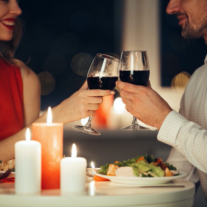 Cropped photo of young lovers having romantic dinner and drinking red wine at home